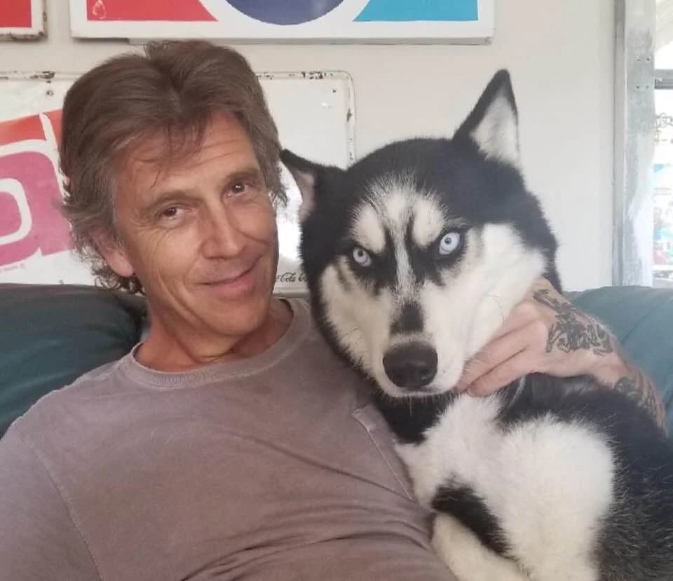 A man relaxes on a couch with a black-and-white Husky nestled close to him