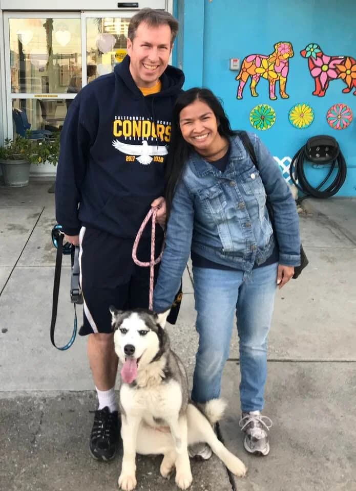 A smiling couple poses with a happy Siberian Husky in front of a colorful pet store mural